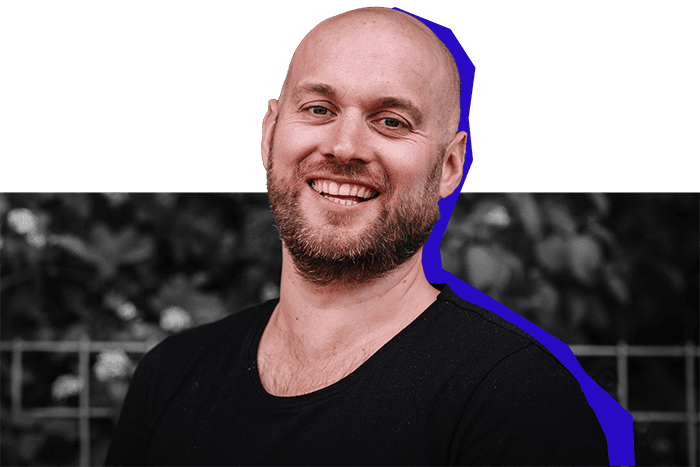Lachende man met zwart T-shirt poseert voor een hek met groene achtergrond, met paarse schaduwrand in uitgesneden stijl.